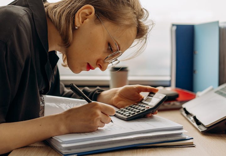 a-woman-writing-on-a-book-while-holding-a-calculator