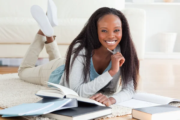 Female student lying on carpet reading books and writing