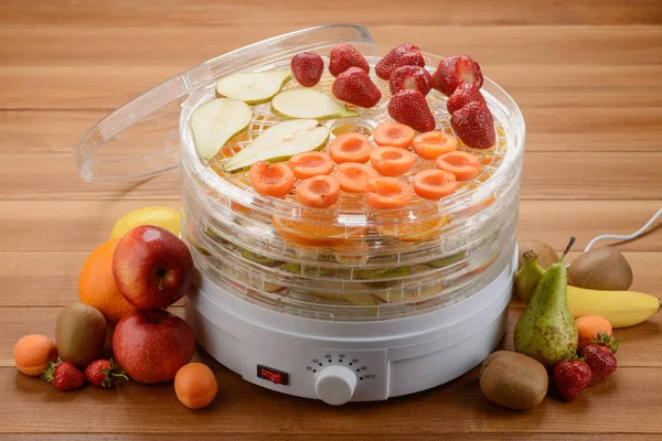 Drying and preserving fruits with an electronic dehydrator. Kitchen tool and heap of various fruits on a wooden table.