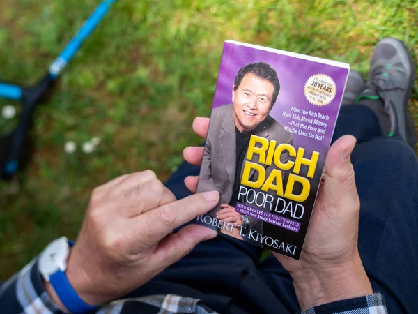 Overhead POV view of senior male hand hodling and readnig the iconic finance book Rich dad and Poor Dad by Robert T Kiyosaki 