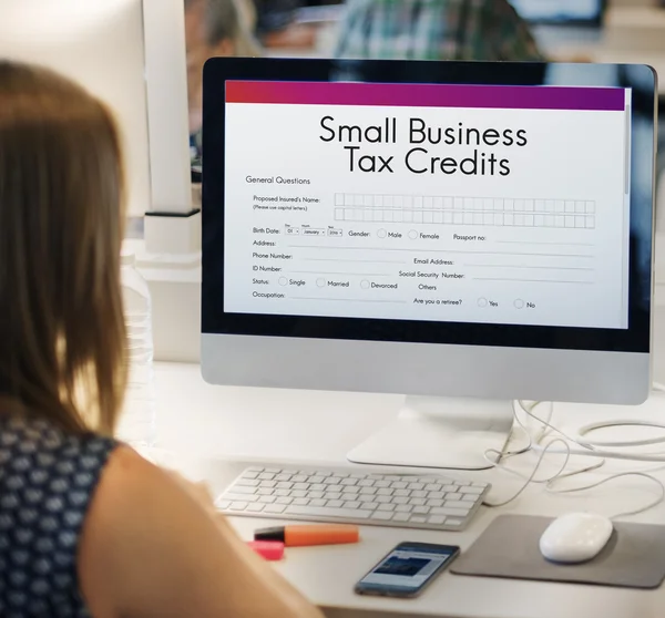 Woman using computer at workplace table, monitor screen with graphic text on screen: Small Business Tax Credits