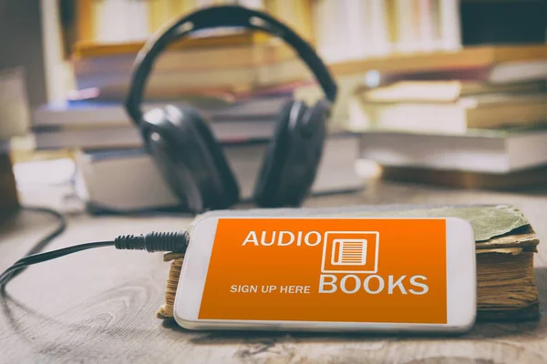 Smart phone with audio books application on screen, headphones and the paper books. Concept of listening to audiobooks.