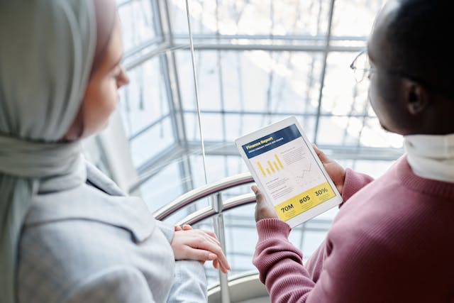Two business professionals discussing financial data on a tablet in a modern office setting